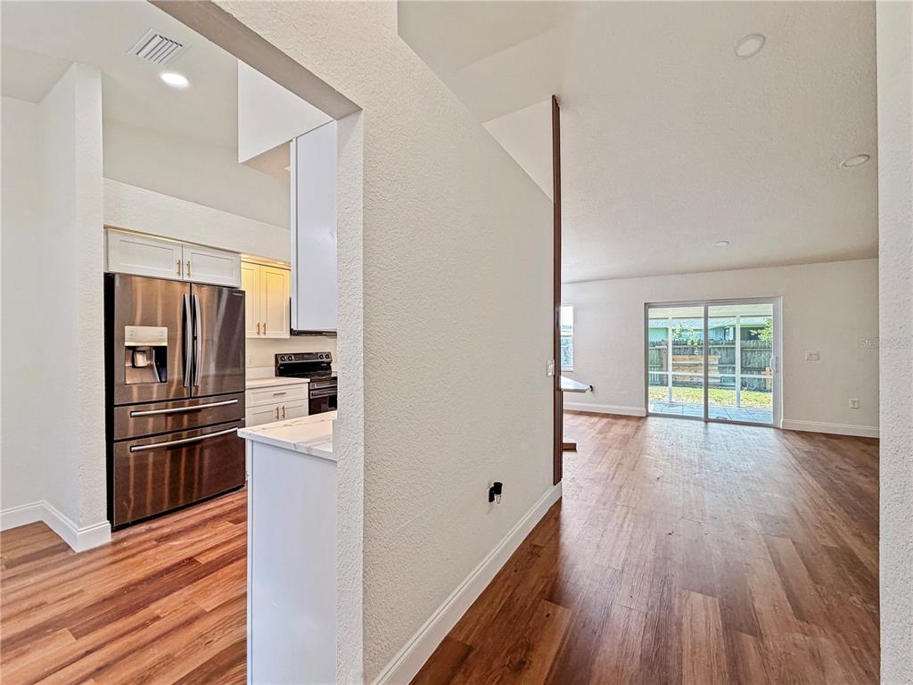 A kitchen with white cabinets, dark appliances, and wood-look flooring leads to a dining area — 2617 SUNDANCE CIRCLE, MULBERRY, FL