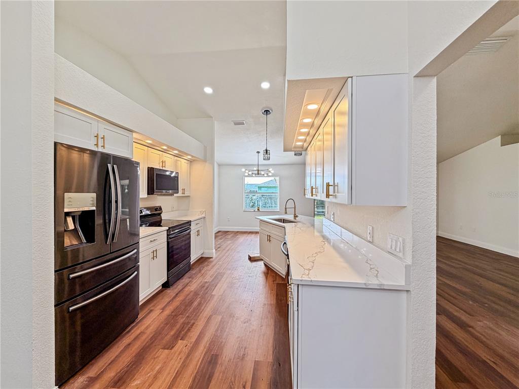 A kitchen with white cabinets, wood-look flooring, and a modern sputnik chandelier — 2617 SUNDANCE CIRCLE, MULBERRY, FL