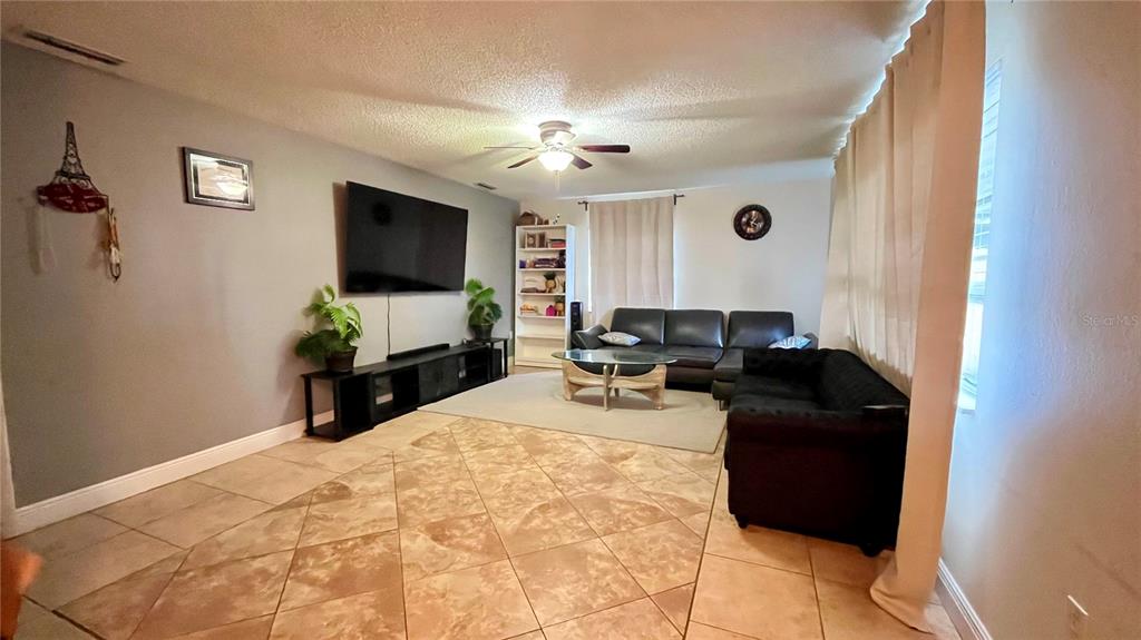 A living room features tile flooring, a large television, and dark leather furniture — 2615 CECILE STREET, KISSIMMEE, FL