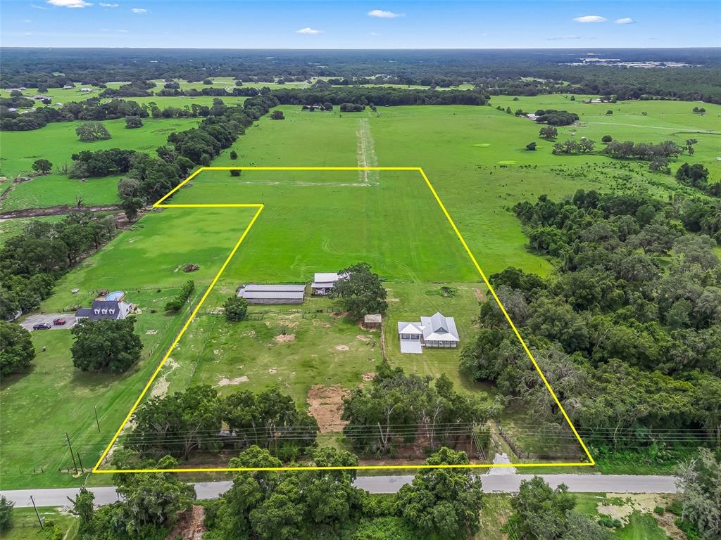 An aerial view shows a rural property with a house, outbuildings, and fenced pasture land — 8567 CR 635, BUSHNELL, FL