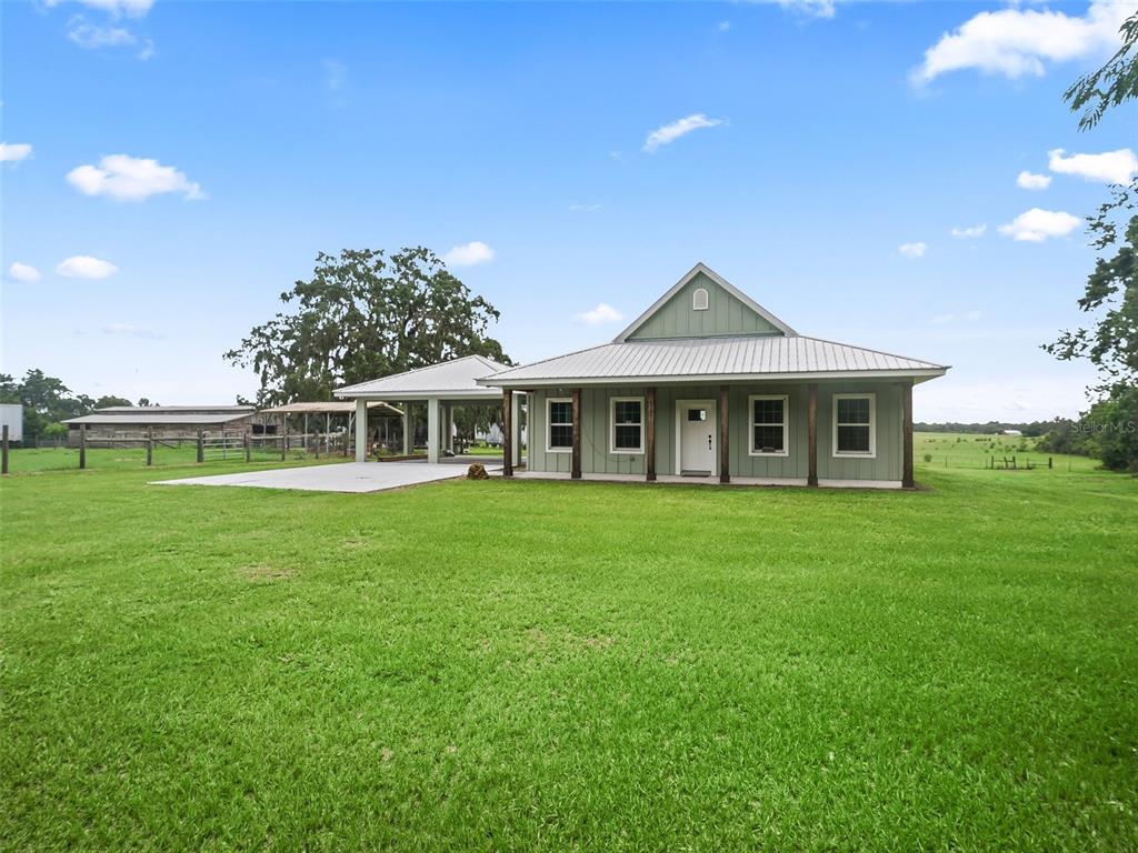 A light green house with a metal roof and a covered carport sits on grass — 8567 CR 635, BUSHNELL, FL