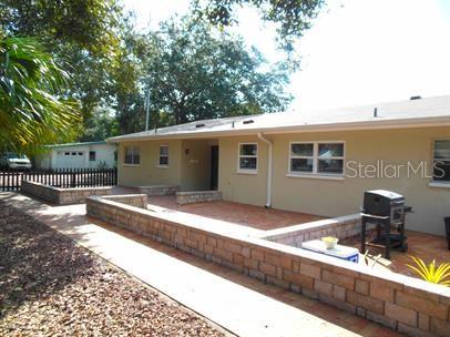 A tan house exterior features a brick patio with a low retaining wall and grill — 7100 DARTMOUTH AVENUE N UNIT 3, ST PETERSBURG, FL