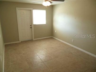 An empty room with beige walls, tile flooring, a ceiling fan, and a white exterior door — 7100 DARTMOUTH AVENUE N UNIT 3, ST PETERSBURG, FL