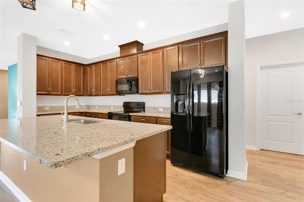 A kitchen with brown wooden cabinets, granite countertops, and black appliances — 2920 MARLBERRY LANE, CLERMONT, FL