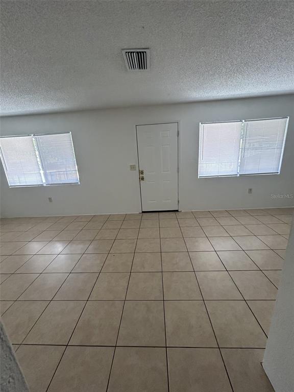 An empty room with beige tile flooring, white walls, two windows, and a central door — 1216 KENNEDY ROAD UNIT 16, DAYTONA BEACH, FL