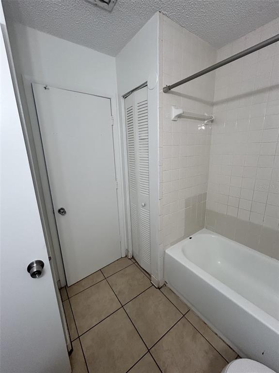 A bathroom features a white bathtub, tiled walls, a louvered closet door, and tiled flooring — 1216 KENNEDY ROAD UNIT 16, DAYTONA BEACH, FL