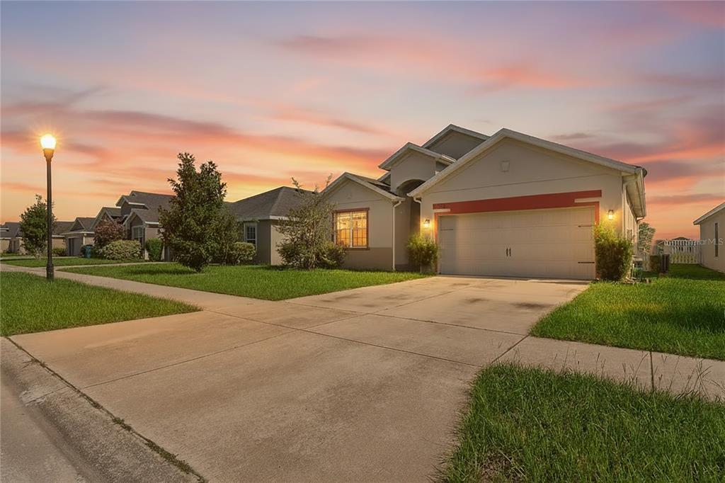 A single-story suburban house with a two-car garage and a concrete driveway at sunset — 30896 SATINLEAF RUN, BROOKSVILLE, FL