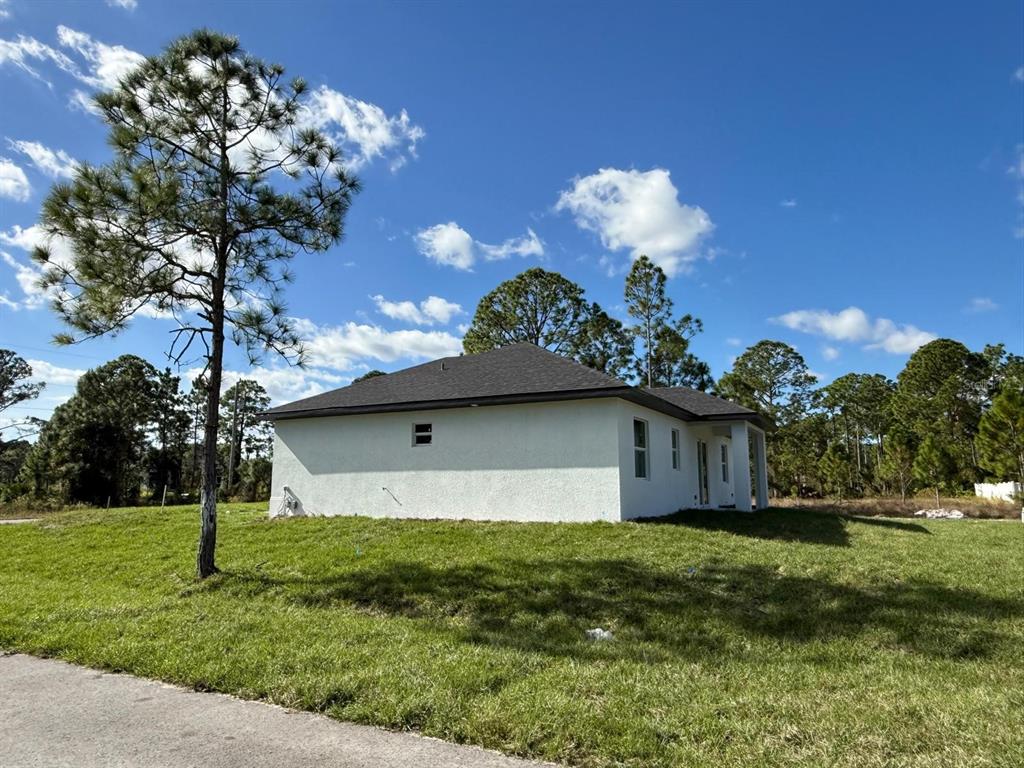 A white stucco house with a dark shingled roof sits on a grassy lot — 1121 FLORENCE STREET E, LEHIGH ACRES, FL