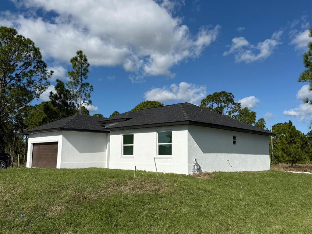 A side view of a white stucco house with a dark roof and garage — 1121 FLORENCE STREET E, LEHIGH ACRES, FL