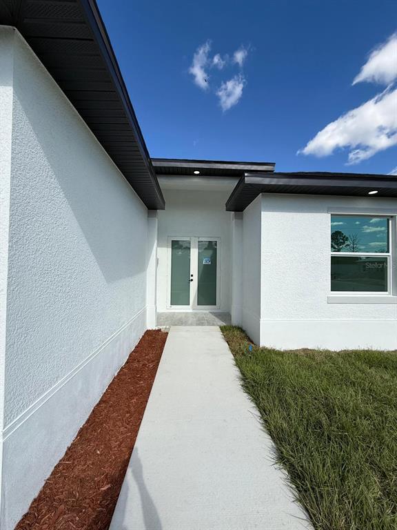 A concrete walkway leads to the double-door entrance of a modern white stucco house — 1121 FLORENCE STREET E, LEHIGH ACRES, FL