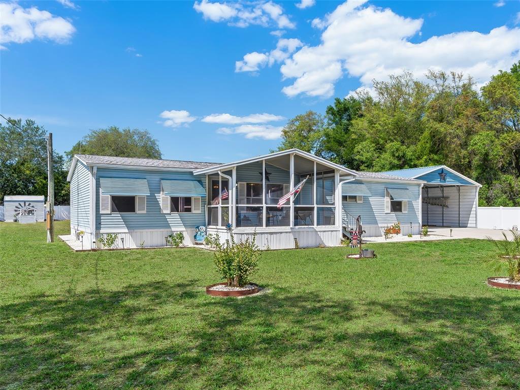 A light blue manufactured home features a screened-in front porch and an attached metal carport — 9975 SE 166TH STREET, SUMMERFIELD, FL