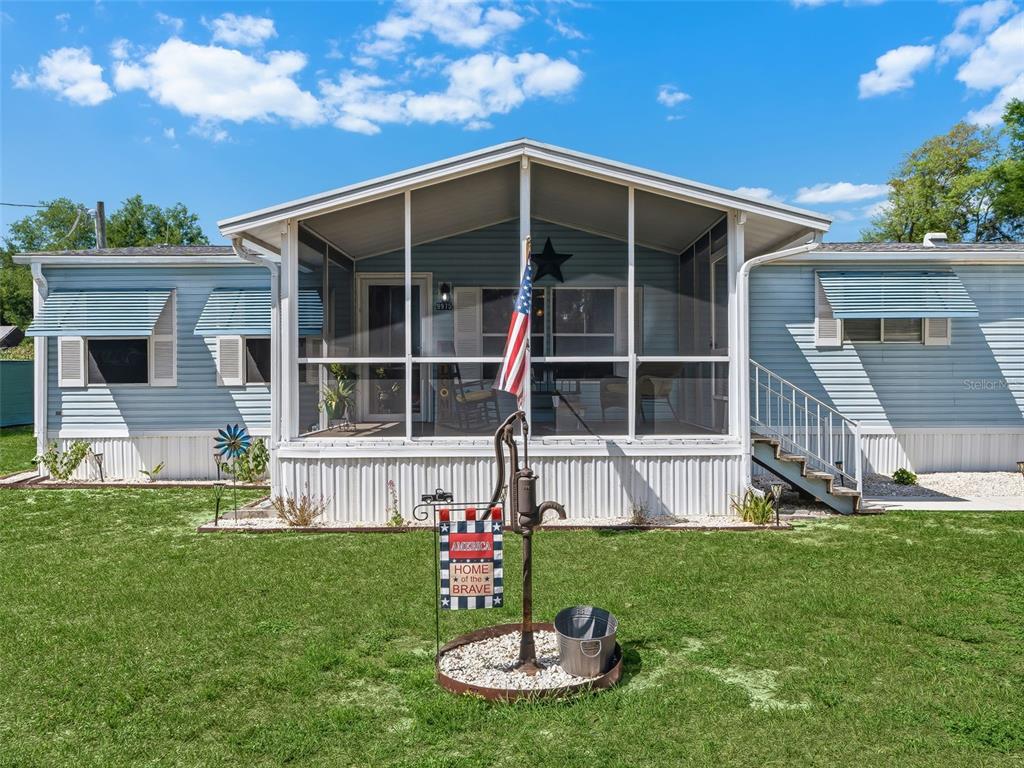 A light blue mobile home features a screened-in front porch and a decorative water pump — 9975 SE 166TH STREET, SUMMERFIELD, FL