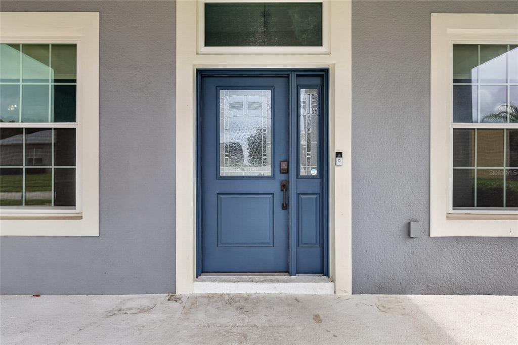A blue front door with a glass insert and sidelight sits between two windows — 5006 RISHLEY RUN WAY, MOUNT DORA, FL