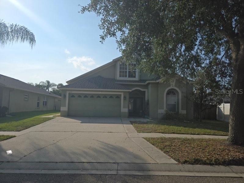 A single-story house with a two-car garage and a large tree in the front yard — 6717 GUILFORD CREST DRIVE, APOLLO BEACH, FL
