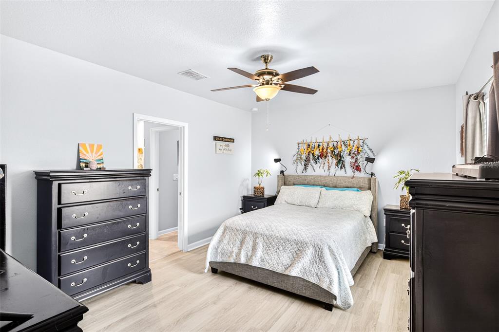 A bedroom features a bed with a floral wall hanging, dark furniture, and light flooring — 617 TROTTERS DRIVE, EAGLE LAKE, FL