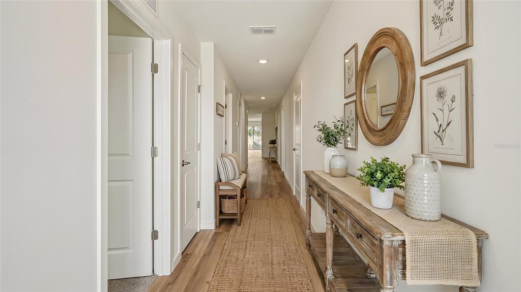 A hallway features wood-look flooring, a wooden console table, a round mirror, and framed art — 1029 COMMONS WAY, PORT ORANGE, FL
