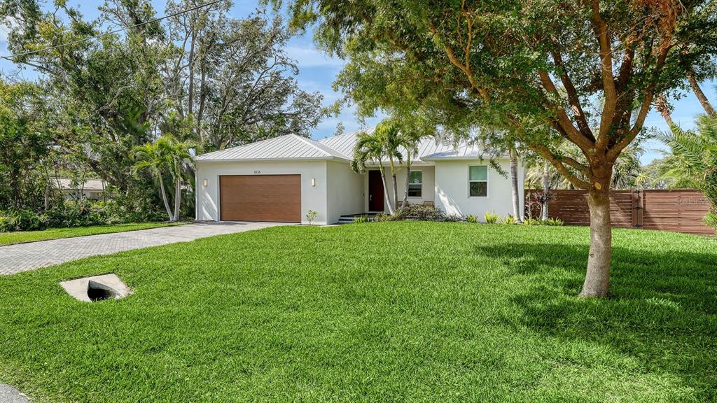 A single-story house with a white exterior, metal roof, and wood-toned garage door — 6136 HOLLYWOOD BOULEVARD, SARASOTA, FL
