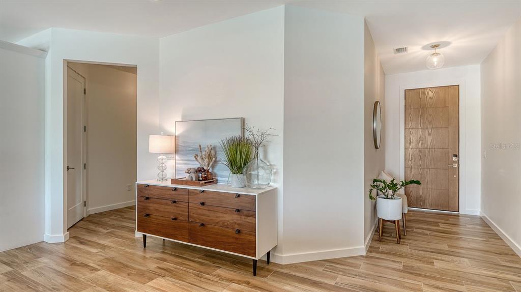 A modern entryway features wood-look tile flooring, a white dresser, and a wooden front door — 6136 HOLLYWOOD BOULEVARD, SARASOTA, FL