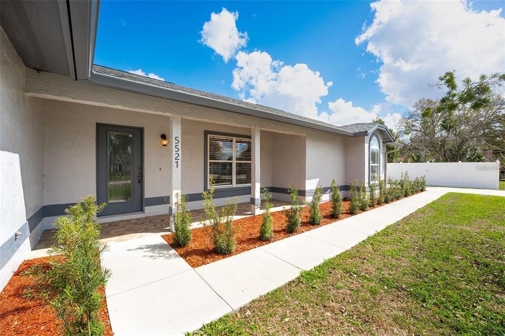 The exterior of a single-story house features a covered porch, a gray door, and landscaping — 5521 OAK STREET, MOUNT DORA, FL