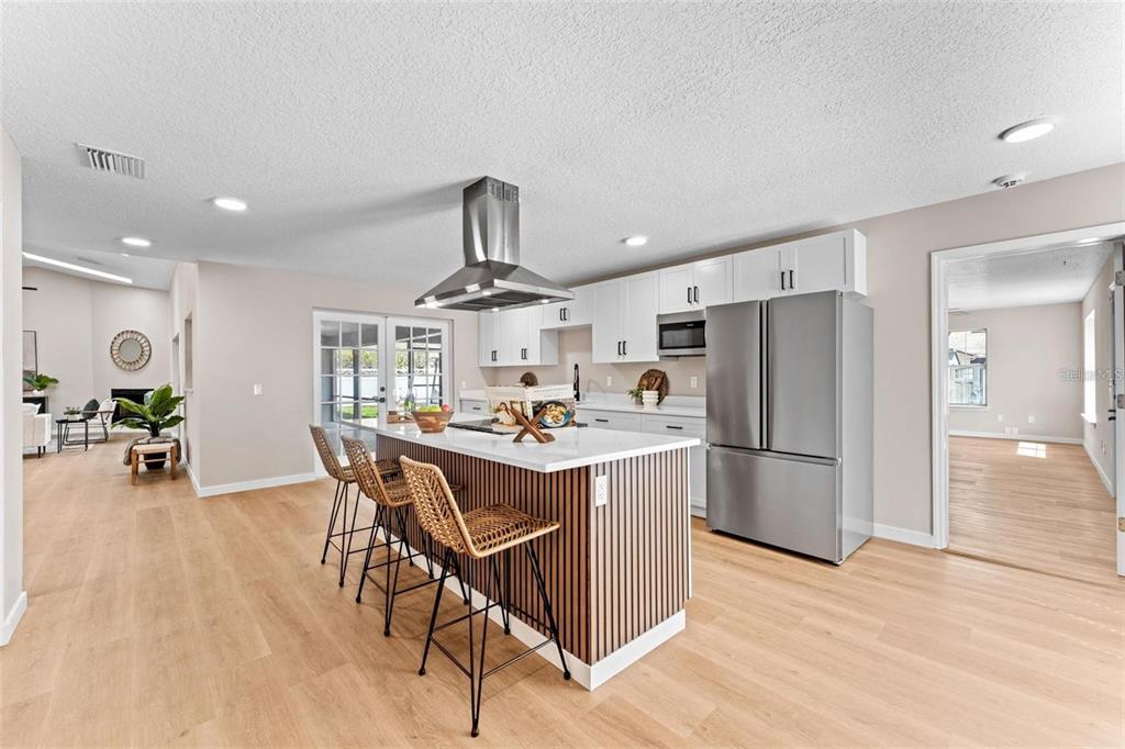 A modern kitchen features a slatted wood island, stainless steel appliances, and light wood flooring — 5521 OAK STREET, MOUNT DORA, FL