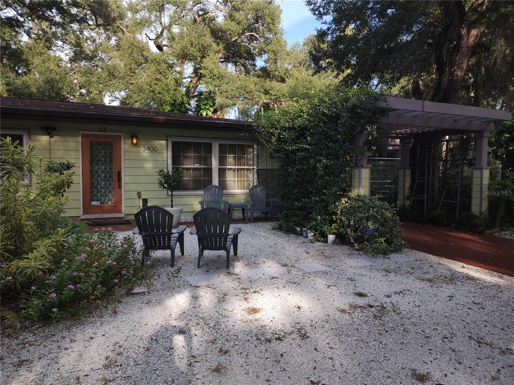 A light green house features a gravel front yard with four dark chairs and a pergola — 3400 CLARK DRIVE, SARASOTA, FL
