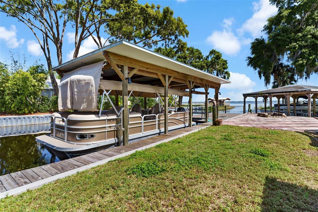 A pontoon boat is docked under a wooden covered slip next to a grassy lawn — 12221 HELENA COURT, LEESBURG, FL