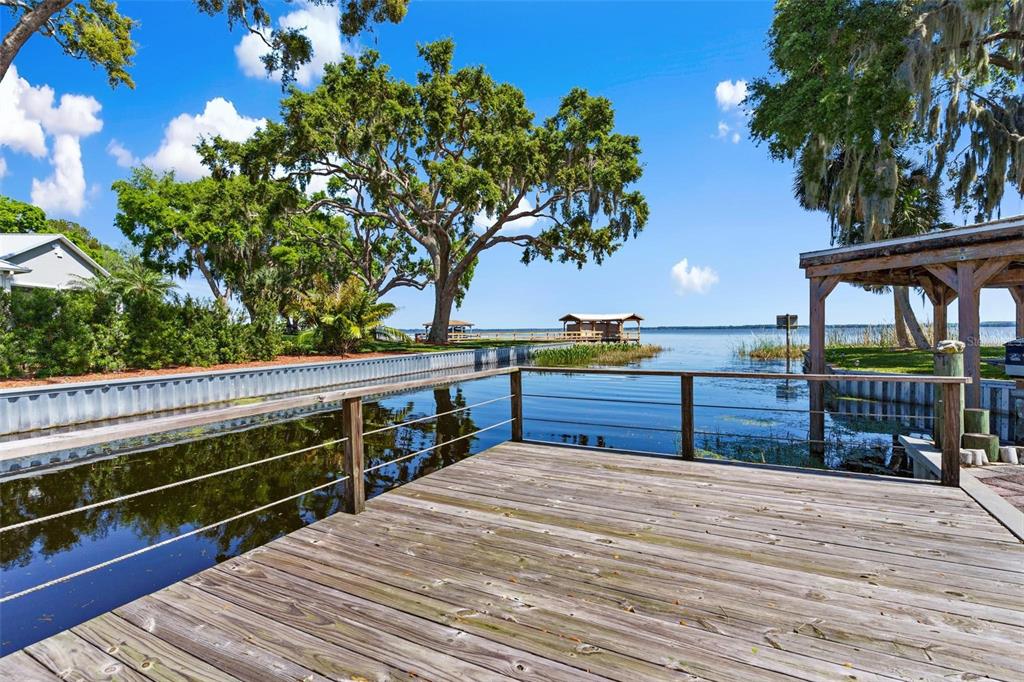 A wooden deck overlooks a canal leading to a lake with a boat dock — 12221 HELENA COURT, LEESBURG, FL