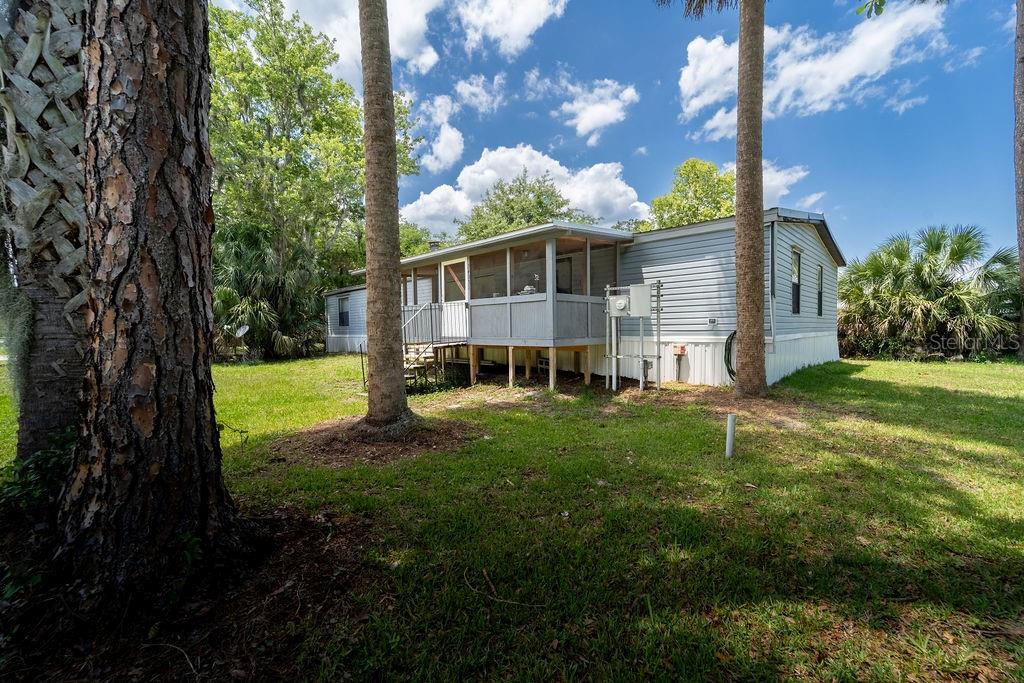 A light blue mobile home with a screened-in porch sits on a grassy lot — 24031 ARMADILLO ROAD, ASTOR, FL