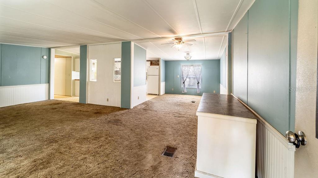 An open-concept living area features blue paneled walls, brown carpeting, and a ceiling fan — 24031 ARMADILLO ROAD, ASTOR, FL