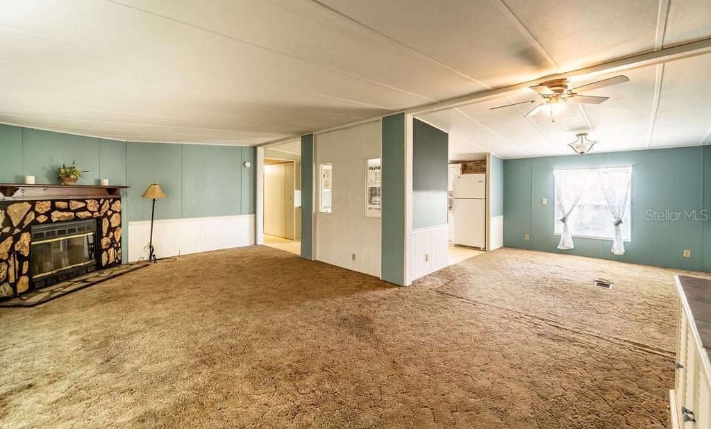 A living room with tan carpet, teal walls, a stone fireplace, and an adjacent kitchen — 24031 ARMADILLO ROAD, ASTOR, FL