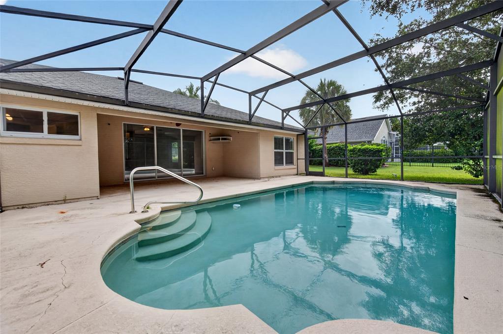 A swimming pool with steps and a handrail sits inside a screened-in patio enclosure — 8 BLACK WATER WAY, ORMOND BEACH, FL