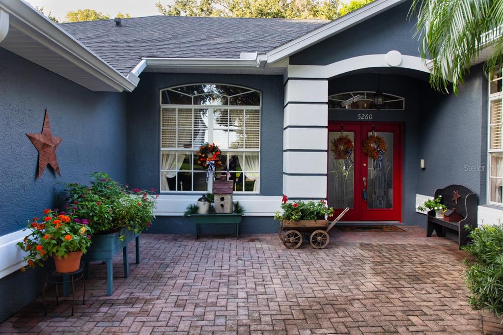 A brick-paved entryway features a dark blue house exterior, a red double door, and planters — 5260 HAMMOCK CIRCLE, ST CLOUD, FL