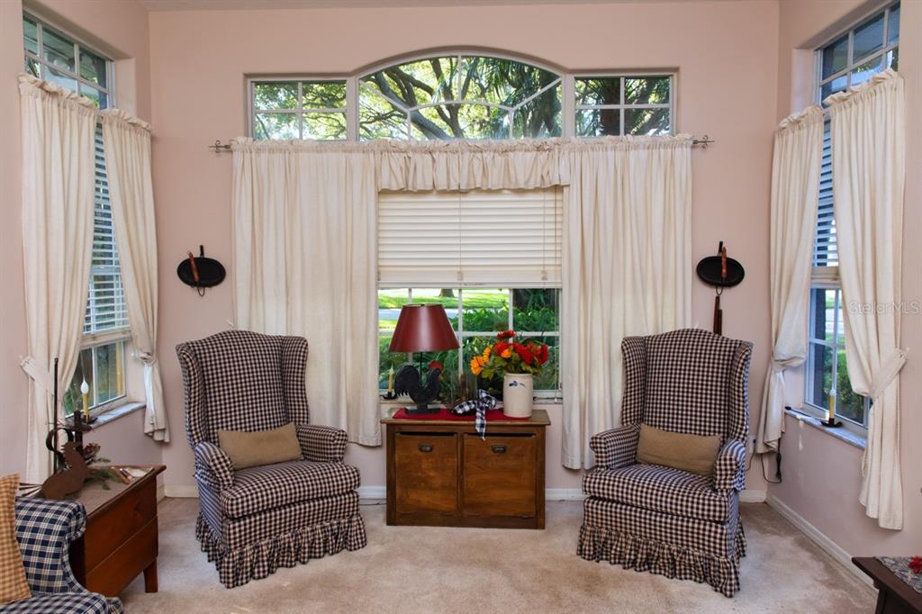 A sunroom features two plaid wingback chairs, a wooden cabinet, and large windows with curtains — 5260 HAMMOCK CIRCLE, ST CLOUD, FL