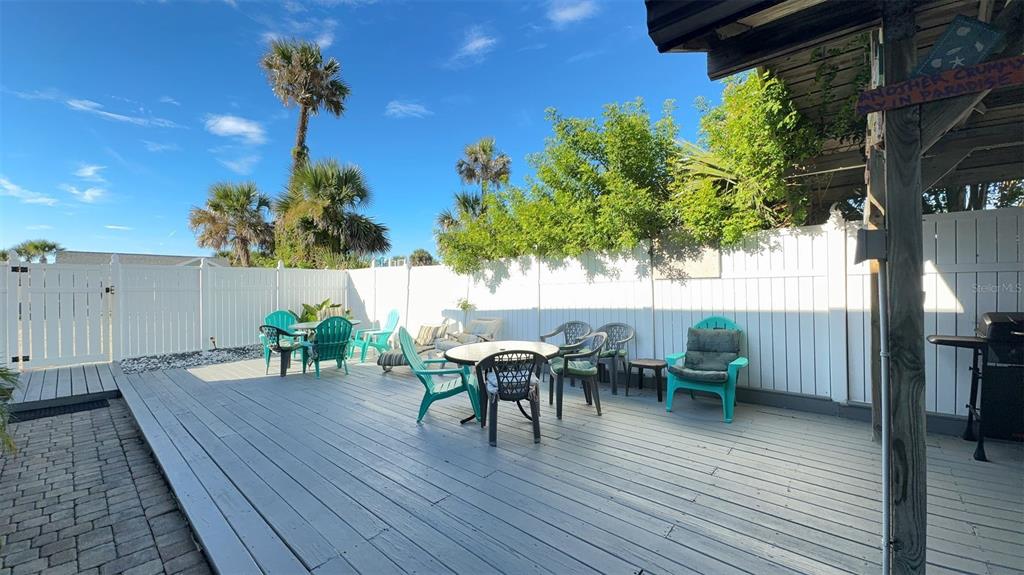 A spacious outdoor wooden deck features multiple seating areas, a white privacy fence, and palm trees — 108 5TH ST SO UNIT 2B, FLAGLER BEACH, FL