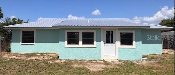 A single-story house with light blue stucco walls and a metal roof under a blue sky — 508 PARK DRIVE, BABSON PARK, FL