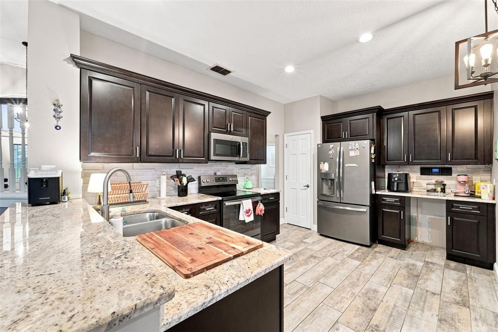A kitchen with dark wood cabinets, granite countertops, stainless steel appliances, and wood-look tile flooring — 3874 GATLIN PLACE CIRCLE, ORLANDO, FL