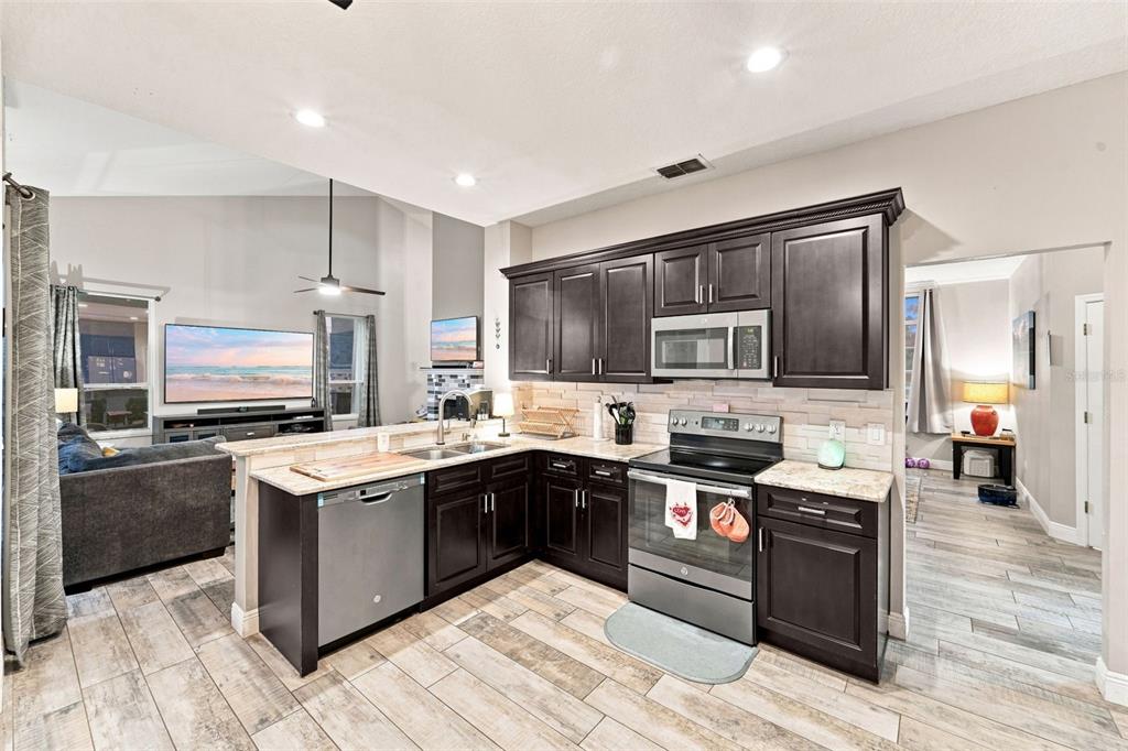 A kitchen with dark wood cabinets, stainless steel appliances, and light countertops overlooks a living area — 3874 GATLIN PLACE CIRCLE, ORLANDO, FL