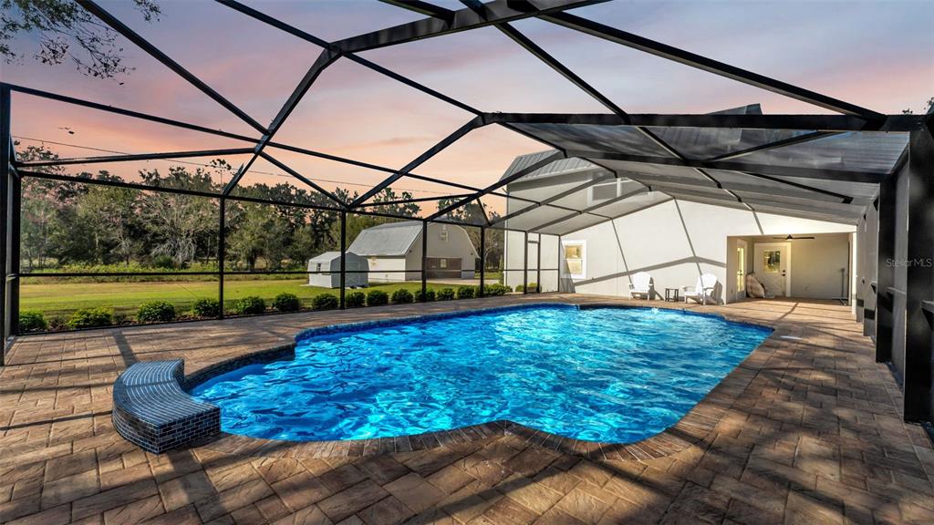 A swimming pool with a tiled deck is enclosed by a screened lanai at sunset — 13 BOGEY DRIVE, WINTER HAVEN, FL