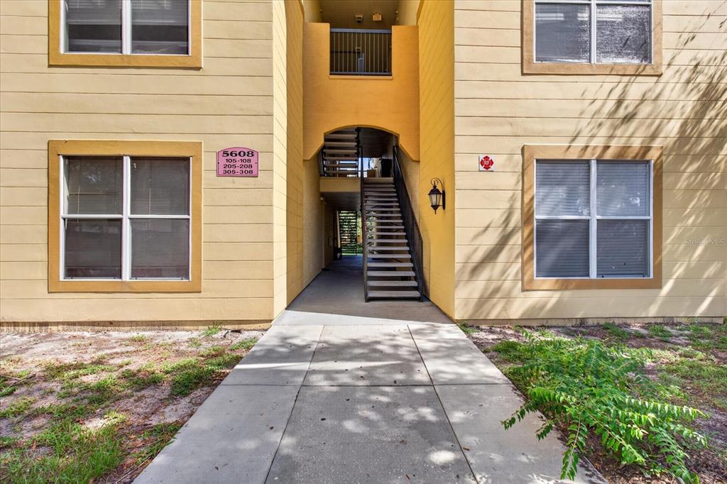 A tan apartment building exterior features a central staircase leading to upper-level units — 5608 PINNACLE HEIGHTS CIRCLE UNIT 305, TAMPA, FL