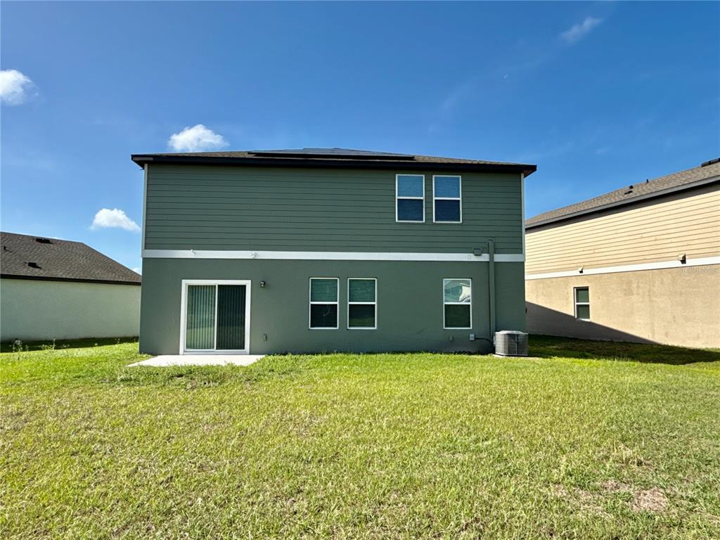 The rear exterior of a two-story green house features a sliding glass door and windows — 35657 BUTTONWEED TRAIL, ZEPHYRHILLS, FL