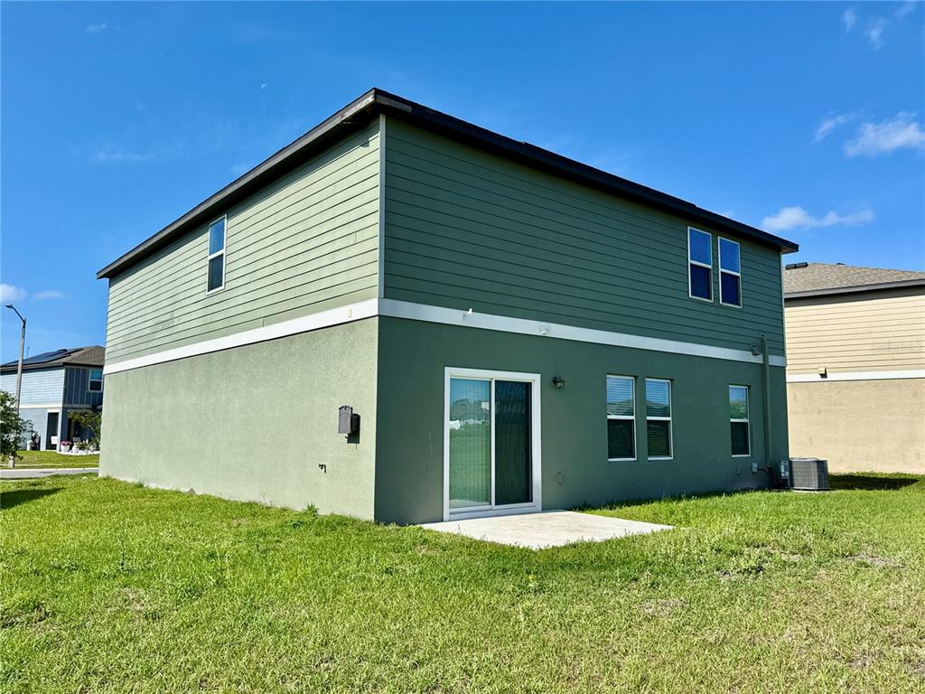 The exterior of a two-story house features green siding, stucco, and a concrete patio — 35657 BUTTONWEED TRAIL, ZEPHYRHILLS, FL