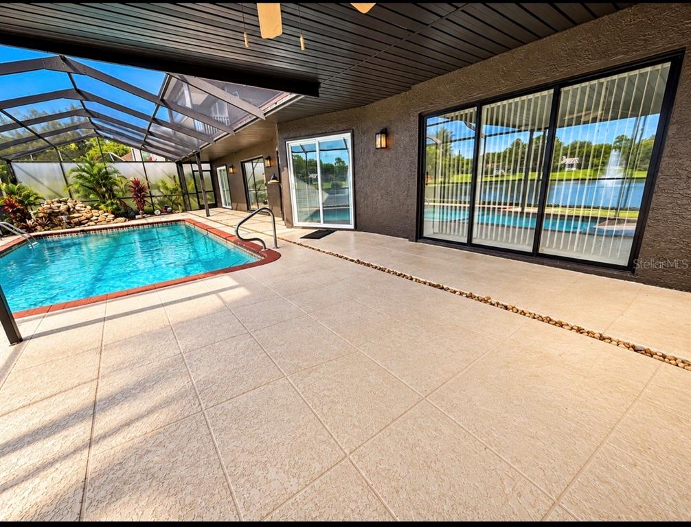 A screened-in patio features a swimming pool, a ceiling fan, and a view of water — 2876 LAKE VALENCIA BOULEVARD E, PALM HARBOR, FL