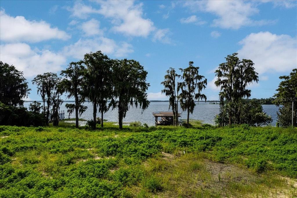 A grassy lot overlooks a lake with several large trees and a wooden boat dock — 12422 PARK AVENUE, WINDERMERE, FL