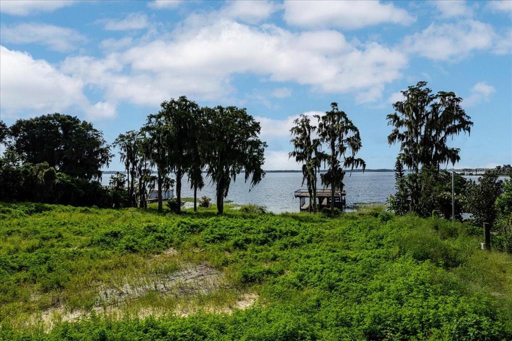 A grassy, overgrown lot leads to a lakefront view with trees and a wooden dock — 12422 PARK AVENUE, WINDERMERE, FL