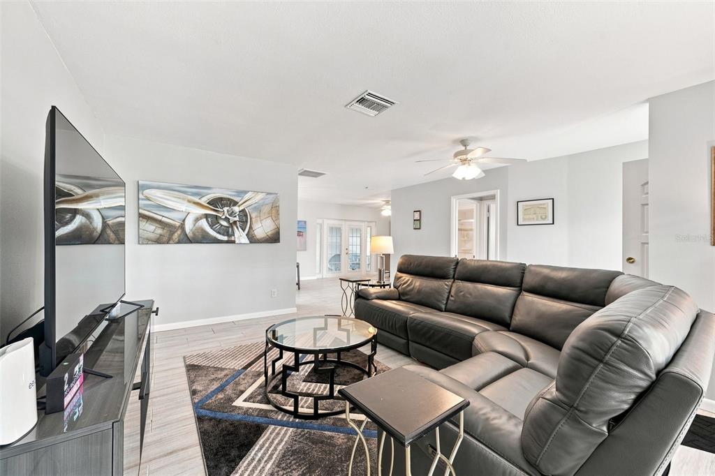 A living room features a dark leather sectional, a glass coffee table, and airplane wall art — 28 WALL TERRACE, REDINGTON SHORES, FL