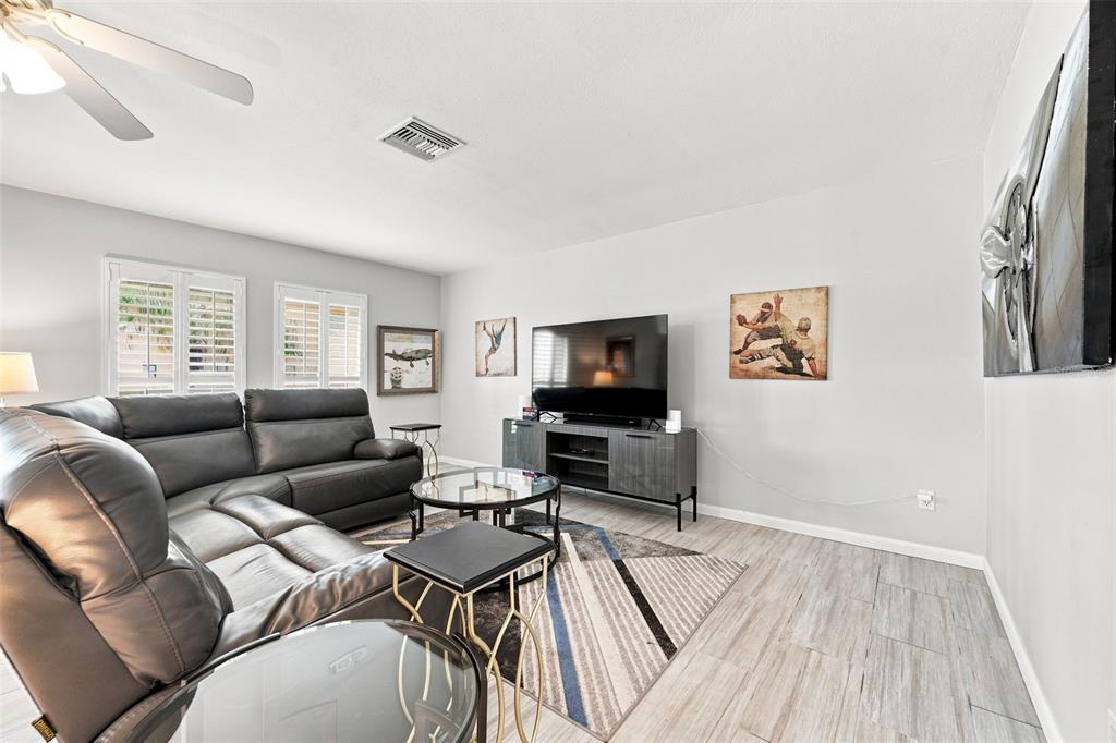 A living room features a gray sectional sofa, a television on a console, and wood-look flooring — 28 WALL TERRACE, REDINGTON SHORES, FL