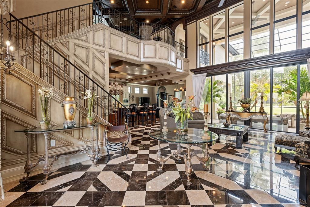 A grand foyer features a curved staircase, black and white marble floors, and floor-to-ceiling windows — 641 WOODBRIDGE DRIVE, ORMOND BEACH, FL