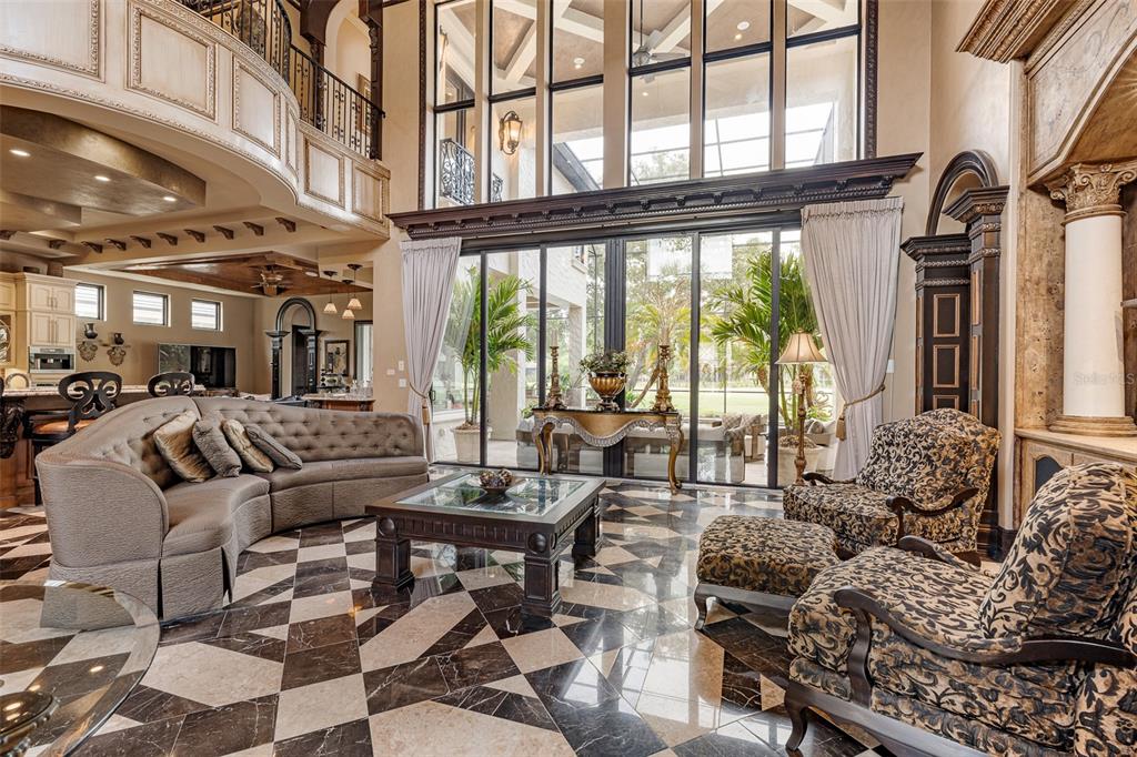 A high-ceilinged living room features a patterned marble floor, a curved sofa, and large windows — 641 WOODBRIDGE DRIVE, ORMOND BEACH, FL