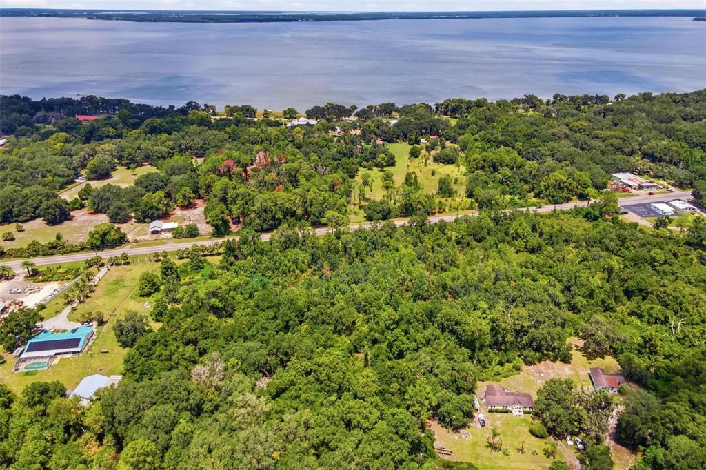 An aerial view shows a large, wooded lot near a lake with several houses nearby — COUNTY ROAD 48, YALAHA, FL