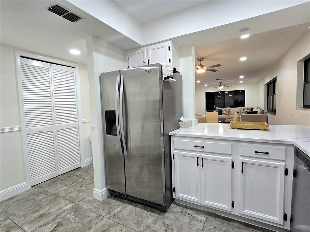A kitchen features white cabinets, a stainless steel refrigerator, and a view into the living room — 2009 HAMMOCK PINE BOULEVARD UNIT 2009, CLEARWATER, FL